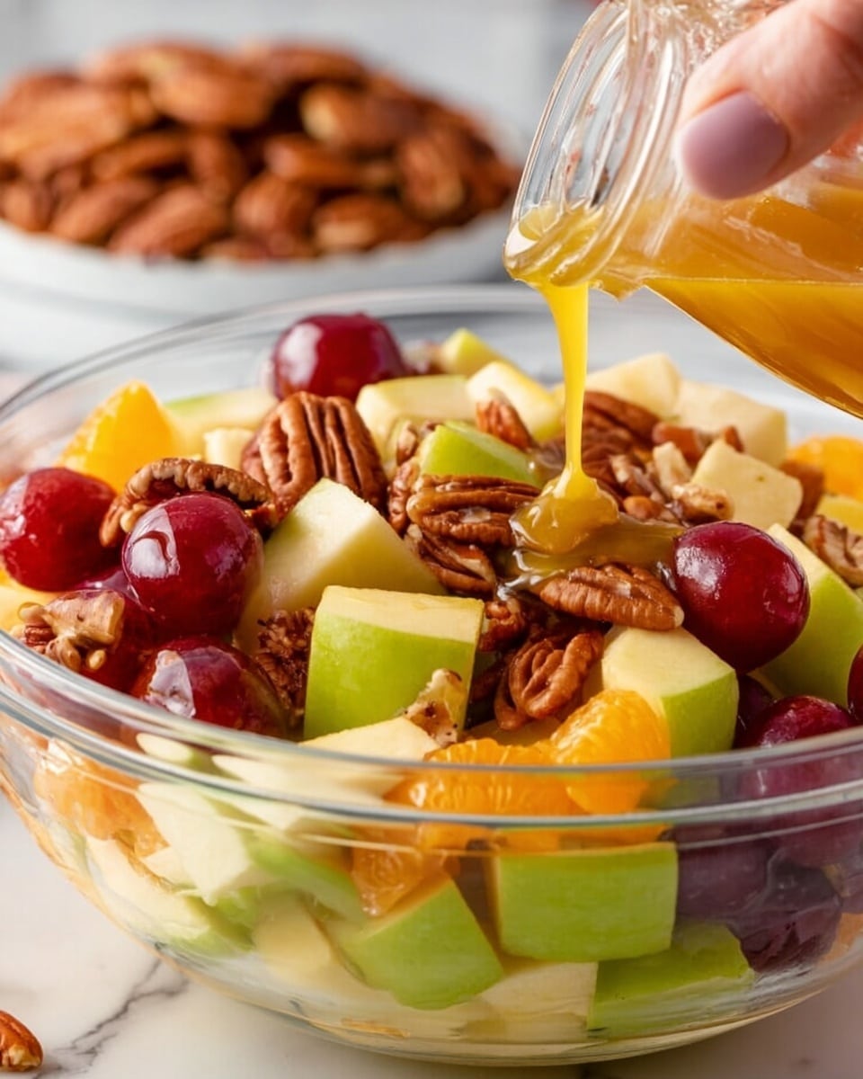 A clear glass bowl filled with a colorful fruit salad that has three main layers: the bottom layer is made of green apple chunks with a smooth surface, the middle layer shows bright orange segments and deep red grapes with shiny skins, and the top layer features light brown pecan halves with a rough texture scattered on top. A woman's hand is pouring a golden dressing over the fruit from a small clear jar, with the dressing flowing in a smooth stream. In the background is a blurred plate of pecans on a white marbled surface. photo taken with an iphone --ar 4:5 --v 7