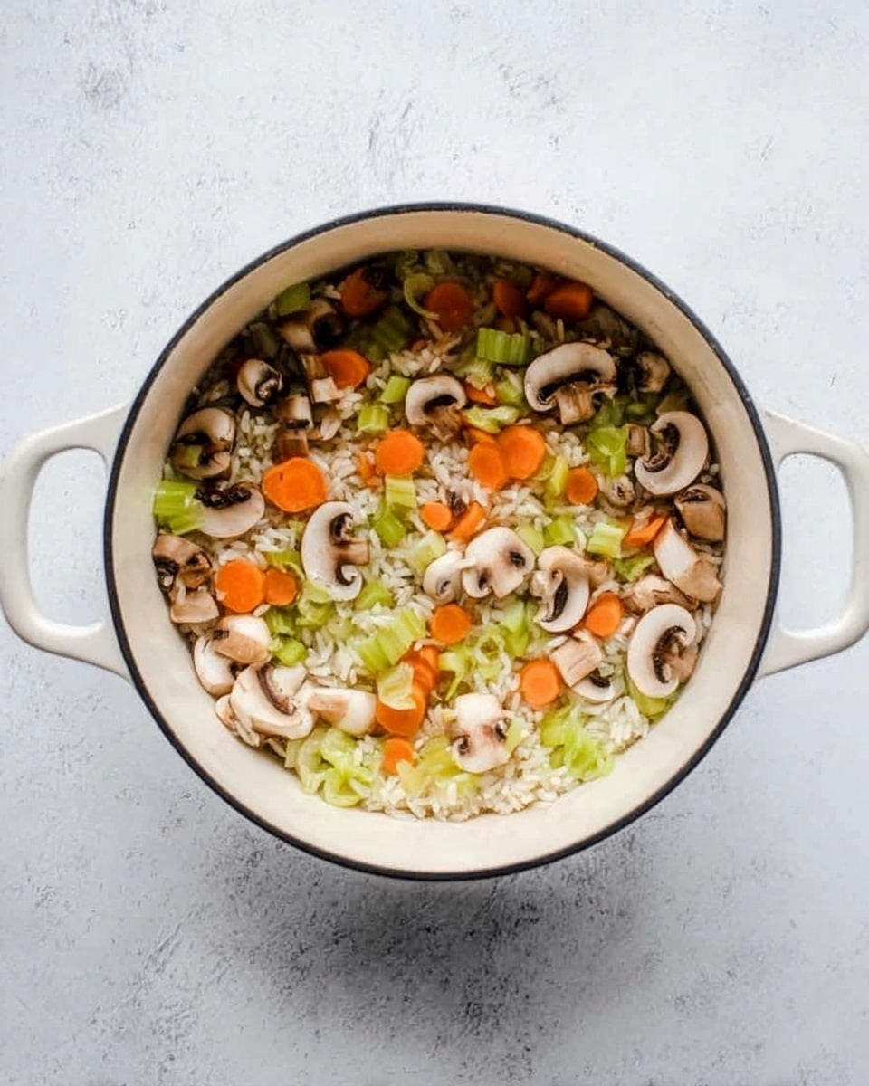 Top view of a white pot filled with layers of raw chopped vegetables and rice on a white marbled surface. The bottom layer is white rice, topped with a mix of thinly sliced light brown mushrooms, bright orange carrot slices, and pale green celery pieces, all scattered evenly across the rice. The pot has two white handles and a black rim around the edge. The overall color mix is natural vegetable tones with a clean white pot and bright background. Photo taken with an iphone --ar 4:5 --v 7
