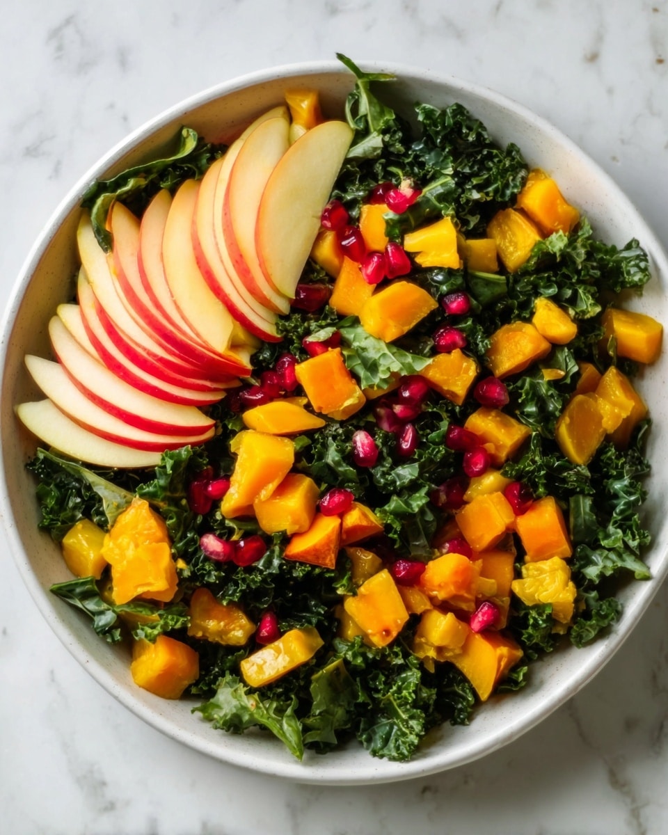 A white bowl filled with a salad made of dark green kale leaves forming the base layer, topped with bright orange chunks of squash scattered all over. On one side inside the bowl, there are several thin slices of pale yellow apple with a light red edge arranged in a small fan shape. Small red pomegranate seeds are scattered on top, providing small spots of bright color. The bowl is placed on a white marbled surface. photo taken with an iphone --ar 4:5 --v 7