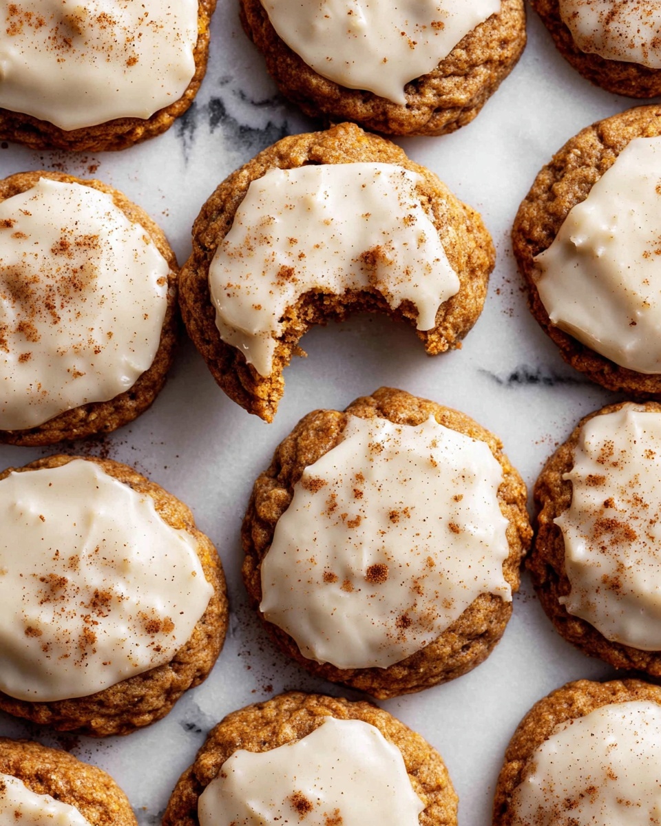 A group of freshly baked cookies arranged closely on a white marbled surface, each cookie has a rough, slightly uneven round shape with deep brown edges and a soft golden-brown center. On top of each cookie is a thick layer of creamy white icing, unevenly spread and glossy, with a light dusting of brown spice powder adding texture and contrast. One cookie near the top center shows a bite taken from it, revealing a moist, dense interior. The overall look is warm and inviting with a rustic homemade style photo taken with an iphone --ar 4:5 --v 7