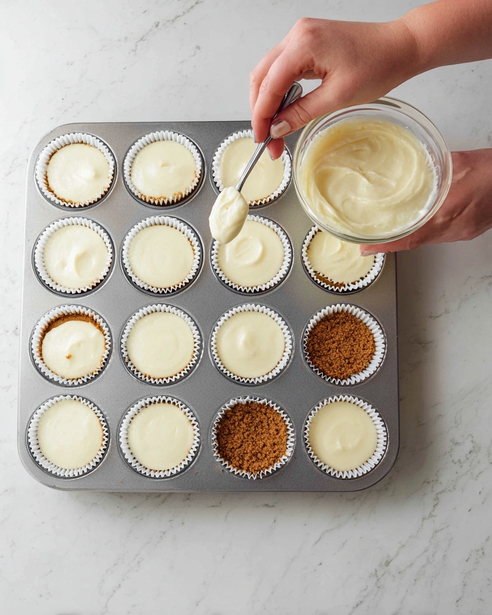 A silver muffin tray filled with twelve white paper liners sits on a white marbled surface. The bottom row shows a crumbly brown crust layer in each liner. The next two rows have a smooth, creamy white filling evenly poured above the crust in all liners. At the top, a woman's hand holds a spoon, spreading the creamy mixture into the last liner, over a plain brown crust. Next to the tray is a transparent round container filled with more of the same creamy white filling. Photo taken with an iphone --ar 4:5 --v 7
