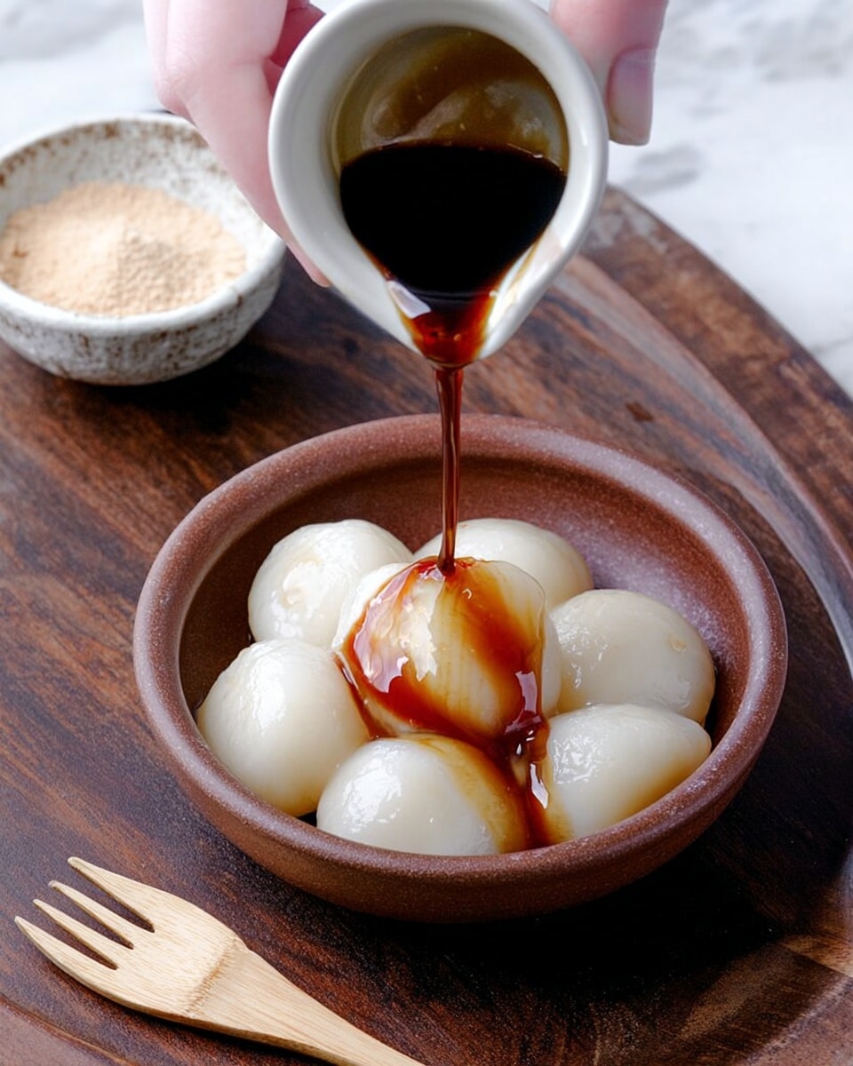 A small brown bowl holds six shiny white dumplings with a smooth surface, arranged in a cluster with some touching. A woman's hand is pouring dark brown syrup from a small white cup that flows over the top dumpling, creating a glossy stream. In the background, there is a small white bowl with a light tan powder and a small light brown wooden fork lies in front of the brown bowl on a dark wooden surface. The photo is taken on a white marbled texture. photo taken with an iphone --ar 4:5 --v 7