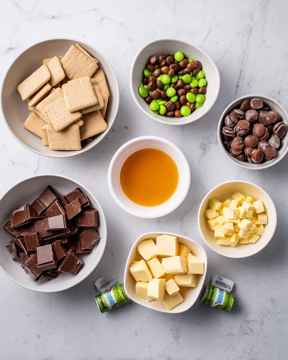 The image shows seven white bowls and one white square bowl arranged on a white marbled surface. The bowls contain different ingredients: one bowl has light beige square-shaped biscuits stacked neatly; another bowl holds small green and brown round candies; two larger bowls contain broken pieces of dark and milk chocolate; a small bowl in the center holds a bright orange liquid; the white square bowl contains yellow butter chunks. A small green and white medicine or food coloring bottle lies on the marble surface below the ingredients. The photo taken with an iphone --ar 4:5 --v 7
