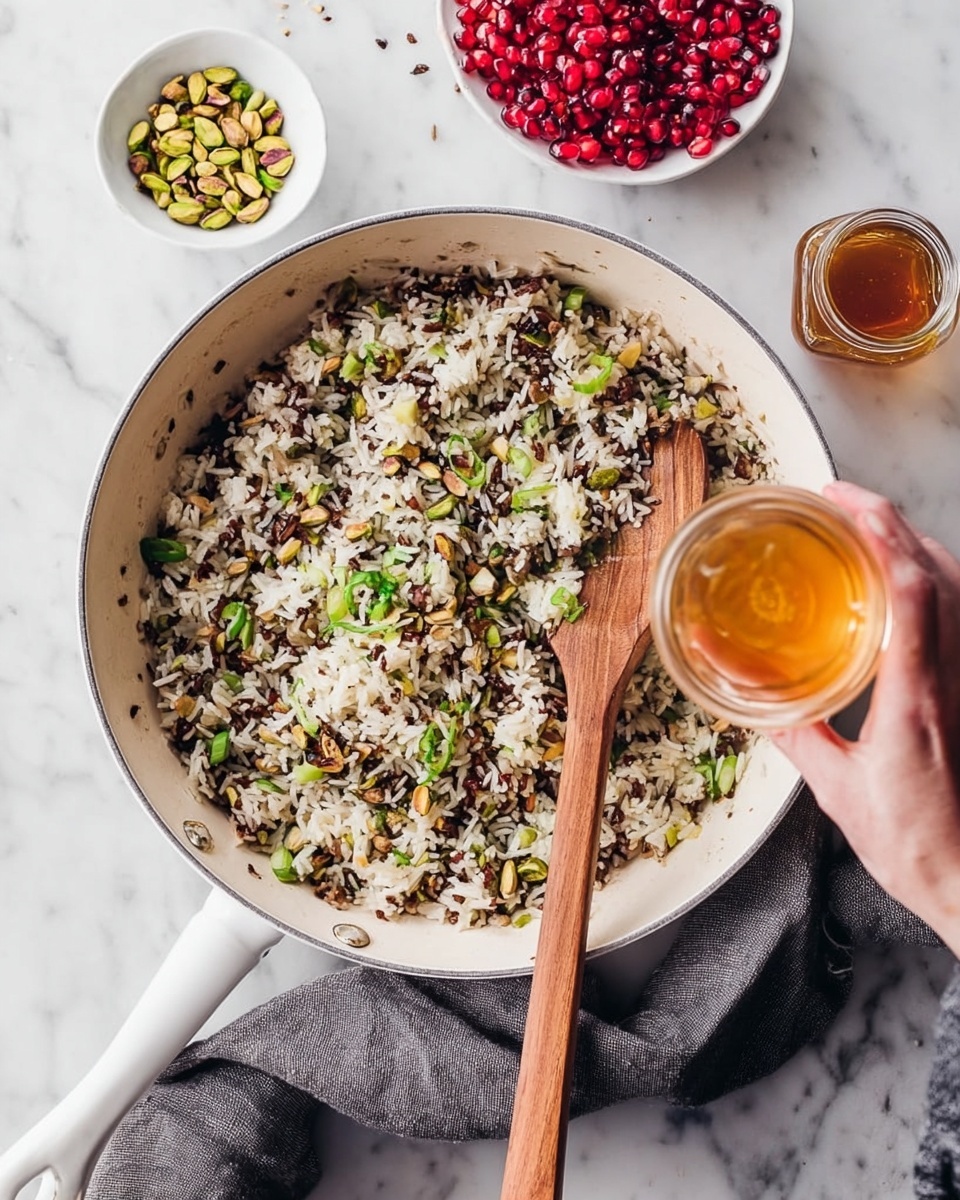 A white pan sits on a white marbled surface with a wooden spoon resting inside it, mixing a dish made of white and brown wild rice with bits of green spring onions scattered through the rice. To the top left are two small white dishes; one contains chopped green pistachios, and the other is filled with bright red pomegranate seeds. A woman's hand is seen holding a small glass jar of golden honey, tilting it over the rice. A gray cloth is placed beneath the handle of the pan. photo taken with an iphone --ar 4:5 --v 7
