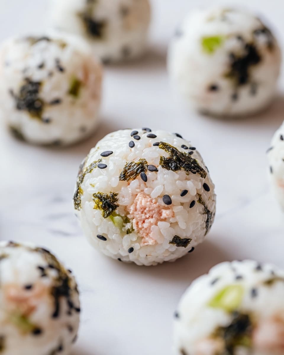 The image shows round sushi balls made of white sticky rice mixed with small black sesame seeds and dark green seaweed flakes. Inside each ball, there is a filling of pinkish fish or seafood with some green vegetable pieces. The sushi balls are placed spaced out on a white marbled surface. The texture of the rice looks soft and slightly shiny, while the seaweed gives a rough contrast. The focus is on one sushi ball in the front center, with blurred sushi balls around it. photo taken with an iphone --ar 4:5 --v 7