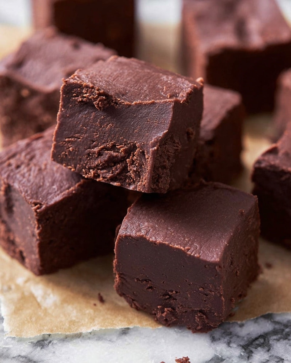 The image shows several thick, square pieces of dark chocolate fudge with a rich, smooth texture and slightly crumbly edges. Each piece is a single layer with a deep brown color, arranged closely together on parchment paper. One piece is slightly tilted, leaning against another, showing the soft, dense inside. The background has a white marbled texture. photo taken with an iphone --ar 4:5 --v 7