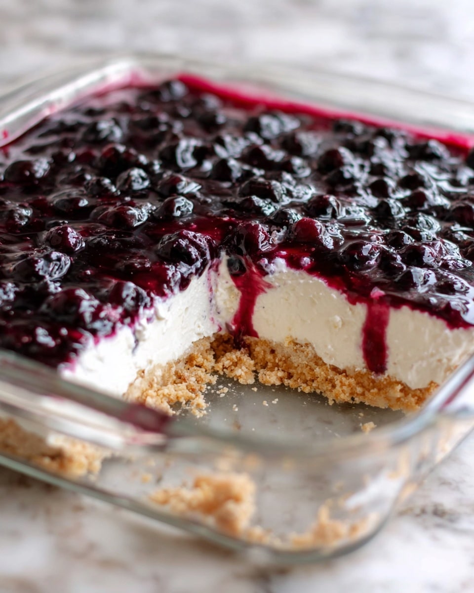 The image shows a square glass dish with a three-layer dessert. The bottom layer is a rough, crumbly light brown crust. The middle layer is smooth, creamy white, and thicker than the crust. The top layer is a shiny, deep purple berry topping with whole dark berries scattered throughout, some juice dripping slightly down the sides of the creamy layer. A section has been taken out from the front left corner, revealing the layers clearly. The dish is placed on a white marbled surface. Photo taken with an iphone --ar 4:5 --v 7