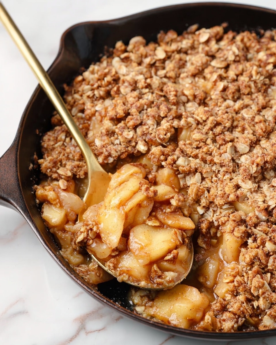A black skillet holds a dessert with two clear layers: the bottom layer is composed of soft, light brown and golden apple chunks mixed with a sticky syrup, while the top layer is a thick, crumbly mixture of oats, nuts, and brown sugar crumbles spread evenly across the surface. A gold spoon scoops a portion from the skillet, revealing the moist fruit layer beneath the crunchy topping. The skillet rests on a white marbled surface. Photo taken with an iphone --ar 4:5 --v 7