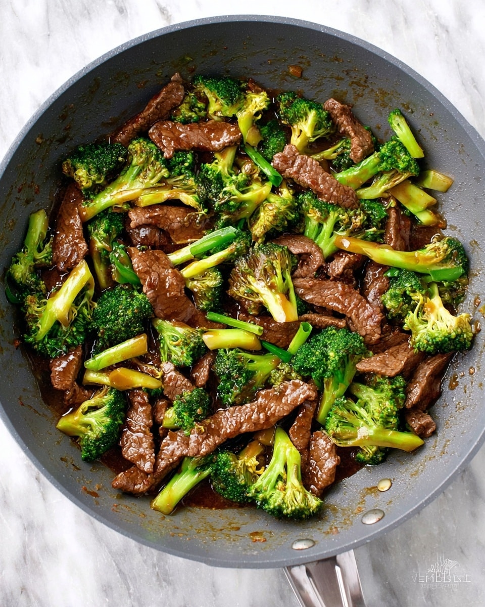 A grey frying pan filled with cooked beef strips and bright green broccoli pieces mixed together, all coated in a glossy brown sauce. The beef slices are thin and uneven, scattered evenly with the broccoli florets which have small stalks attached. The surface beneath the pan is a white marbled texture. Photo taken with an iphone --ar 4:5 --v 7