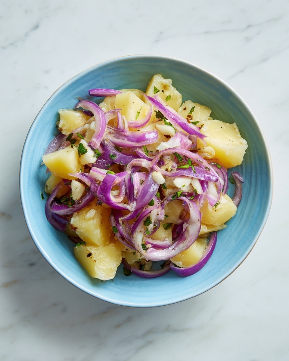 A light blue bowl holds a simple dish with two layers. The bottom layer is made of chunky light yellow potato pieces with a soft, slightly smooth texture. The top layer features thinly sliced red onion rings scattered unevenly, adding a vibrant purple color and crisp texture. Small bits of white garlic and sprinkled green herbs sit on top, adding contrast and freshness. The bowl is placed on a white marbled surface. Photo taken with an iphone --ar 4:5 --v 7