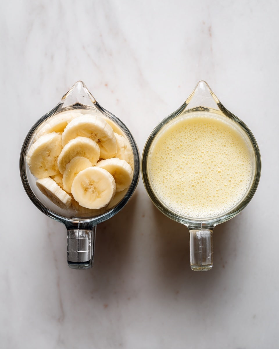 The image shows two clear glass measuring cups placed side by side on a white marbled surface. The left measuring cup contains several slices of pale yellow bananas, positioned at the bottom. The right measuring cup shows a light creamy yellow liquid, smooth and foamy, filling about the same level as the banana slices in the left cup. A metal hammer is positioned above the left measuring cup, suggesting the fruit was mashed or pressed. The background remains clean and bright with the white marble texture. photo taken with an iphone --ar 4:5 --v 7