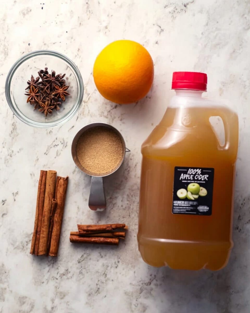 The image shows a white marbled surface with a clear glass bowl holding star anise on the upper left, below it three brown cinnamon sticks placed horizontally, and next to them an orange fruit. Above the orange, there is a metal measuring cup filled with light brown ground spice. On the right side of the arrangement is a large plastic jug filled with brown apple cider, with a red cap and a black label reading
