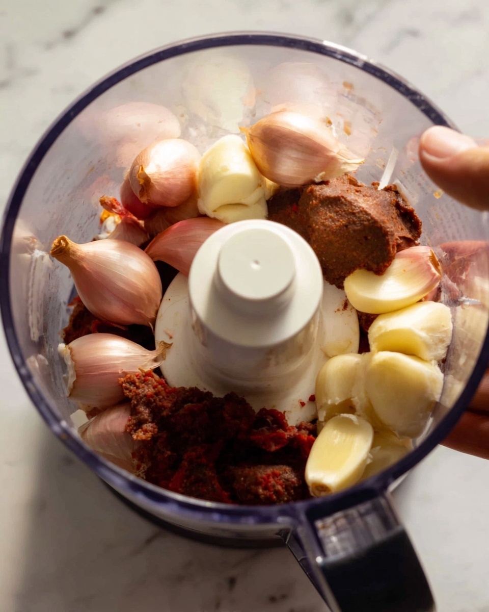 A clear food processor bowl filled with several garlic cloves, whole shallots with light pinkish skin, and chunky pieces of red-brown tamarind pulp around the white blade in the center. A woman's hand is visible at the top edge, holding the bowl. The scene is set on a white marbled surface. photo taken with an iphone --ar 4:5 --v 7