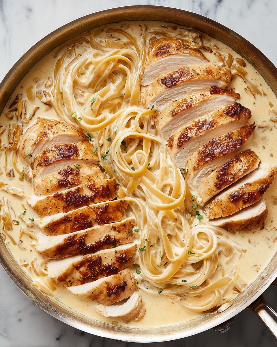 Two sliced, golden-brown cooked chicken pieces are placed on top of long, thick noodles that are covered in a creamy light beige sauce. The dish sits in a round metal pan, with the noodles partly visible beneath the chicken, showing a smooth, rich texture mixed with the sauce. The background is a white marbled surface. photo taken with an iphone --ar 4:5 --v 7