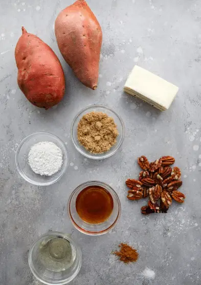 The image shows three whole orange sweet potatoes on a white marbled surface, surrounded by small white bowls containing various ingredients. From top left to right, there are two whole garlic cloves, a few garlic pieces, small green parsley leaves in a bowl, butter cubes in another bowl, and a bowl of white creamy yogurt or sour cream with a bit of red seasoning. Below these are grated yellow cheese in a bowl, a small bowl with yellow cornmeal or polenta, and a bowl of white salt. The colors are warm and natural, with the arrangement neat and visually clear, all placed on the white marbled surface photo taken with an iphone --ar 4:5 --v 7