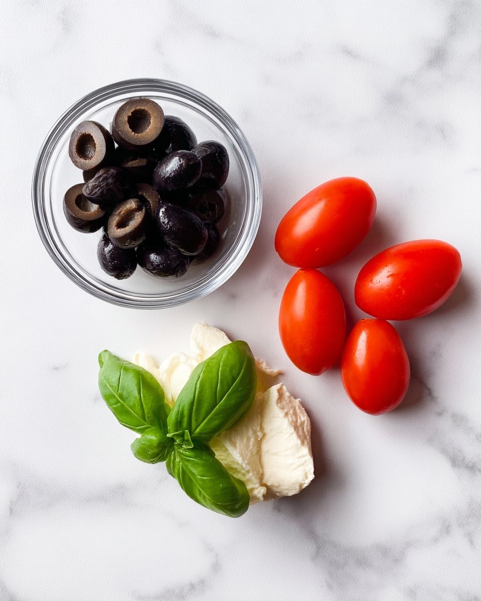 The image shows a simple arrangement on a white marbled surface. In the top left is a small clear glass bowl filled with sliced black olives, showing their dark purple-black color and smooth texture. To the right, there are four small, oval red tomatoes with a shiny, smooth skin clustered together in a loose group. Below the bowl and tomatoes, there is a dollop of white creamy cheese with a soft, spreadable texture. On top of the cheese sits a fresh, bright green basil leaf with a smooth, slightly shiny surface. Photo taken with an iphone --ar 4:5 --v 7