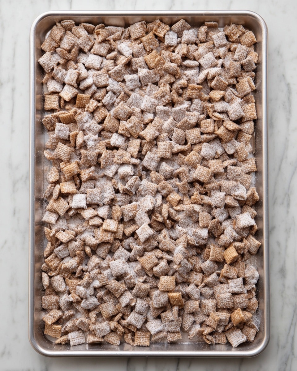 A large rectangular baking tray filled with a single even layer of small, square-shaped cereal pieces covered in a fine white powder. The cereal pieces have a light brown color with a slightly rough texture. The baking tray is placed on a white marbled surface. photo taken with an iphone --ar 4:5 --v 7