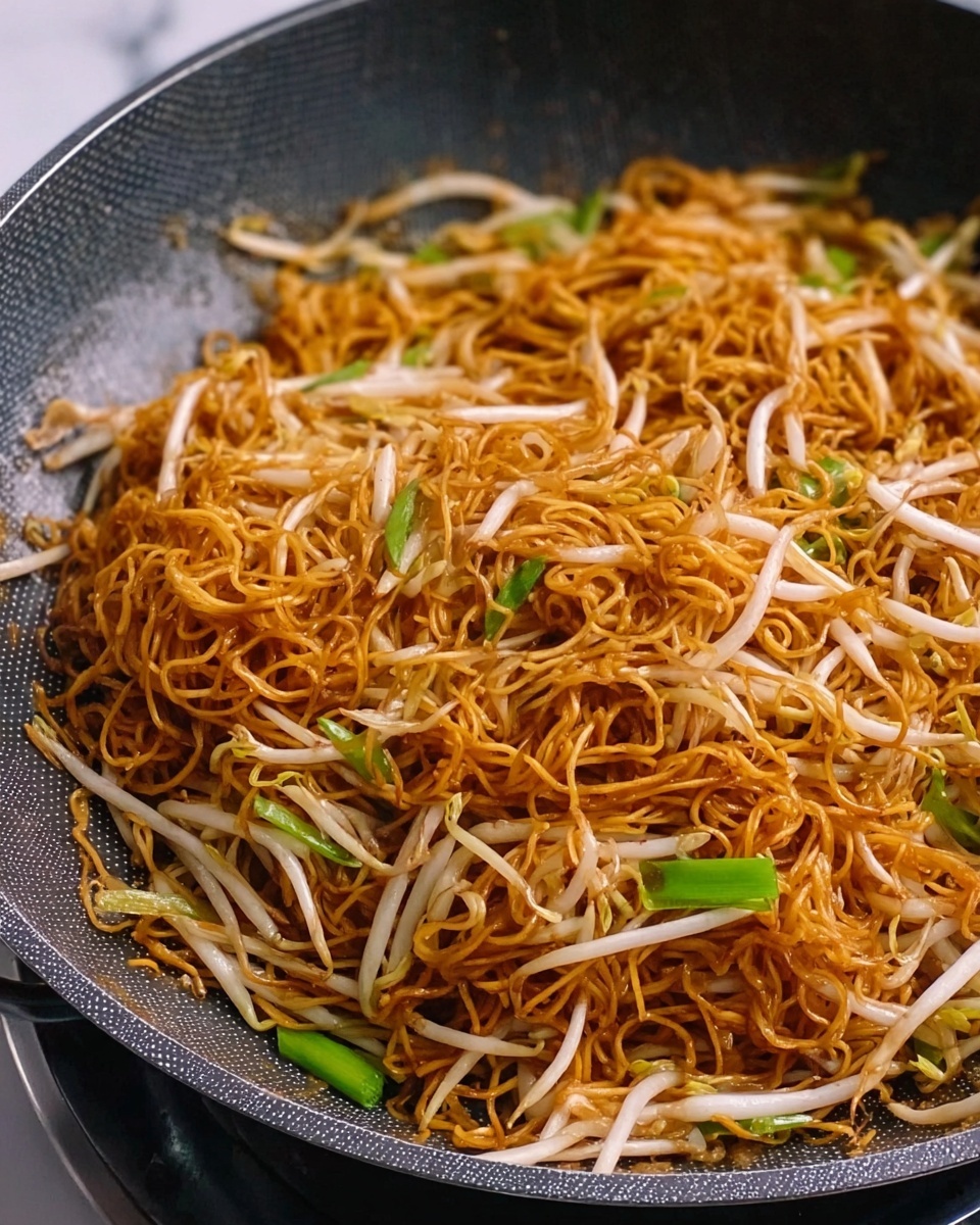 The image shows a pan filled with thin, cooked noodles that have a golden brown color, mixed with light-colored bean sprouts and a few green onion pieces scattered throughout. The noodles are slightly tangled and have a shiny texture from the sauce, lying evenly across the bottom of the pan. The pan itself is dark gray with a textured surface inside. The background is a white marbled texture photo taken with an iphone --ar 4:5 --v 7
