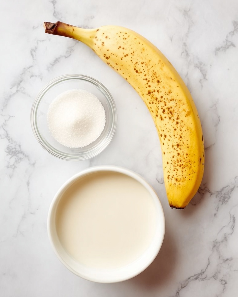 A ripe yellow banana with brown spots lies curved on a white marbled surface at the top right. Below it, in the center, is a small clear glass bowl filled with white sugar. At the bottom, a larger white bowl holds a creamy white liquid, filling most of the bowl’s space. The three items are arranged vertically in a simple, clean layout photo taken with an iphone --ar 4:5 --v 7
