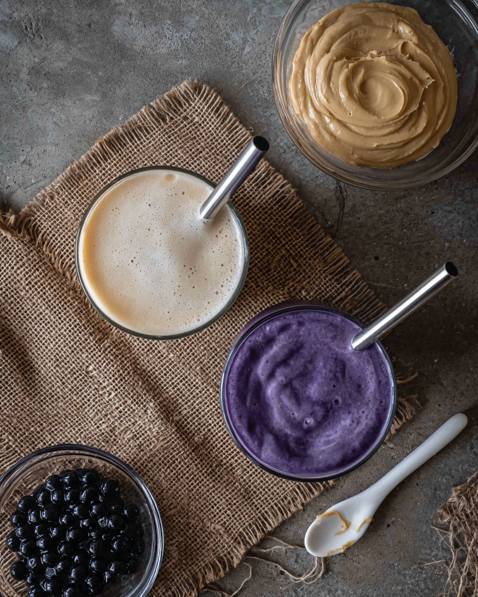 The image shows two glasses of drinks placed on a rough brown woven cloth on a grey rough surface. One glass has a light cream colored drink with a frothy top, and the other glass has a smooth purple drink with a creamy surface. Both glasses contain silver metal straws. On the top right side, there is a clear bowl filled with a beige creamy paste, and a white spoon with some of the same paste rests nearby on the surface. At the bottom left corner, a clear bowl contains dark black round boba pearls. The overall setting is casual with natural textures and sparse elements. Photo taken with an iphone --ar 4:5 --v 7