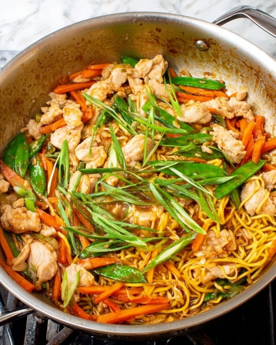 A large silver pan filled with a colorful stir fry dish sits on a stove. The stir fry has several layers, starting with thin orange carrot strips and yellow noodles at the bottom. On top of these are chunks of light beige cooked chicken and bright green snow peas. The dish is garnished with long, thin green onion pieces spread evenly across the top. The pan is slightly shiny and has some brown sauce stains around the edges. The background surface is a white marble texture. photo taken with an iphone --ar 4:5 --v 7
