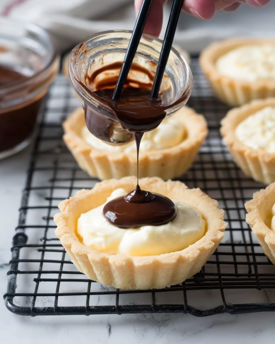The image shows a close-up of a small tart with a light golden crust and creamy white filling, sitting on a black wire rack over a white marbled surface. Above the tart, a woman's hand holds black chopsticks dipping into a clear glass bowl filled with shiny dark chocolate sauce, gently pouring the chocolate over the center of the creamy filling. More tarts with the same crust and filling are visible in the background along with the bowl of chocolate. The whole scene has soft lighting highlighting the smooth textures of the cream and glossy chocolate. Photo taken with an iphone --ar 4:5 --v 7