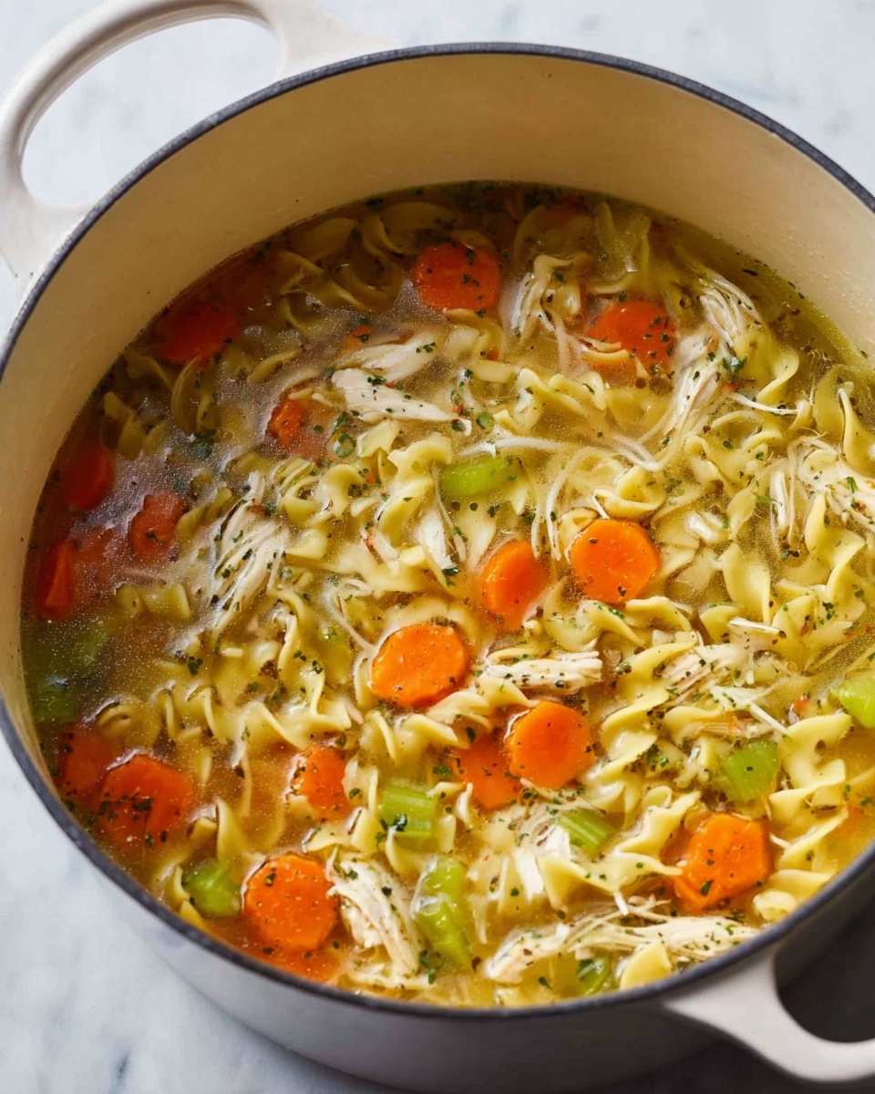 A white pot filled with clear chicken broth soup, showing layers of light yellow egg noodles spread throughout the dish. Bright orange carrot slices and light green celery pieces float evenly in the broth. Shredded white chicken meat is scattered across the surface, mixed with herbs and small pieces of seasonings. The white pot sits on a white marbled surface, creating a clean and fresh look. photo taken with an iphone --ar 4:5 --v 7
