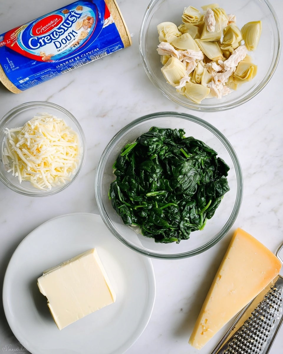 The image shows several ingredients arranged neatly on a white marbled surface. In the center is a clear glass bowl filled with cooked green spinach, showing a soft and slightly wet texture. Above it, there is another clear glass bowl containing small pieces of pale yellow artichoke hearts mixed with white shredded chicken. To the left side, a small clear glass bowl holds shredded white cheese. Below that, on a white plate, is a neat square block of cream cheese with a smooth and creamy texture. On the upper left corner lies a blue and red cylinder container labeled