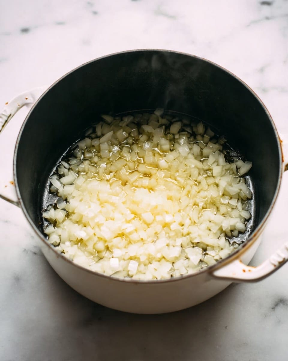 Inside a white pot with a dark inside, there is a single layer of small white chopped onions being cooked. The pot is placed on a white marbled surface. Steam rises gently from the onions, which look soft and are starting to turn translucent. The pot handle on the right side is visible with a bit of wear on it. Photo taken with an iphone --ar 4:5 --v 7