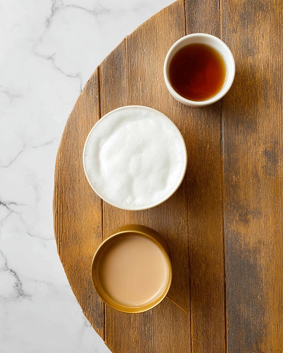 The image shows a top view of a wooden table with three items arranged in a triangular shape. In the center is a white cup filled with a foamy white drink, showing a smooth texture on the surface. On the top right, there is a small white cup filled with a dark amber liquid, likely tea. At the bottom left, there is a gold cup holding a creamy light brown liquid with a slight froth on top. The background is a white marbled texture. photo taken with an iphone --ar 4:5 --v 7