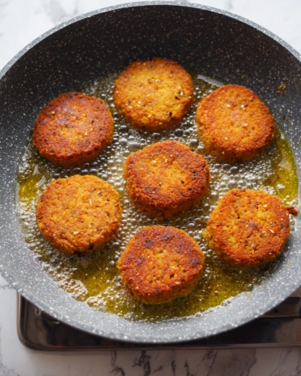 The image shows seven golden brown round patties frying evenly in a non-stick grey speckled pan with bubbling oil around them. The patties have a crispy, crunchy texture with small bits visible on their surface. The pan is placed on a stove with a metal edge visible at the bottom. The background is a white marbled surface. photo taken with an iphone --ar 4:5 --v 7
