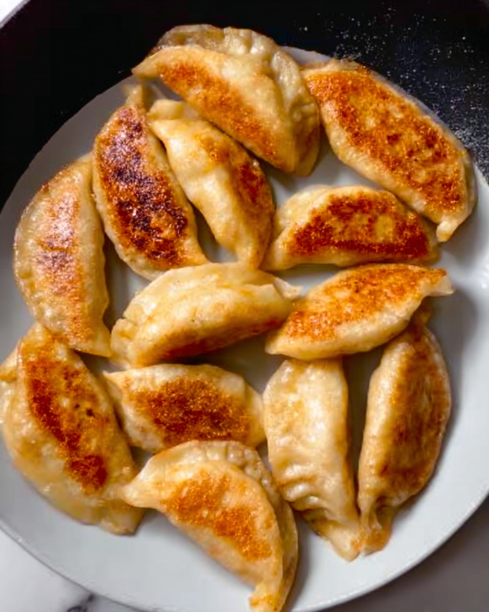 A white plate filled with several golden brown and light tan dumplings arranged in a slightly overlapping way. The dumplings have smooth, slightly shiny skins with some areas showing a crispy, browned texture. The dumplings are shaped like small half-moons. The plate is set on a white marbled surface. photo taken with an iphone --ar 4:5 --v 7