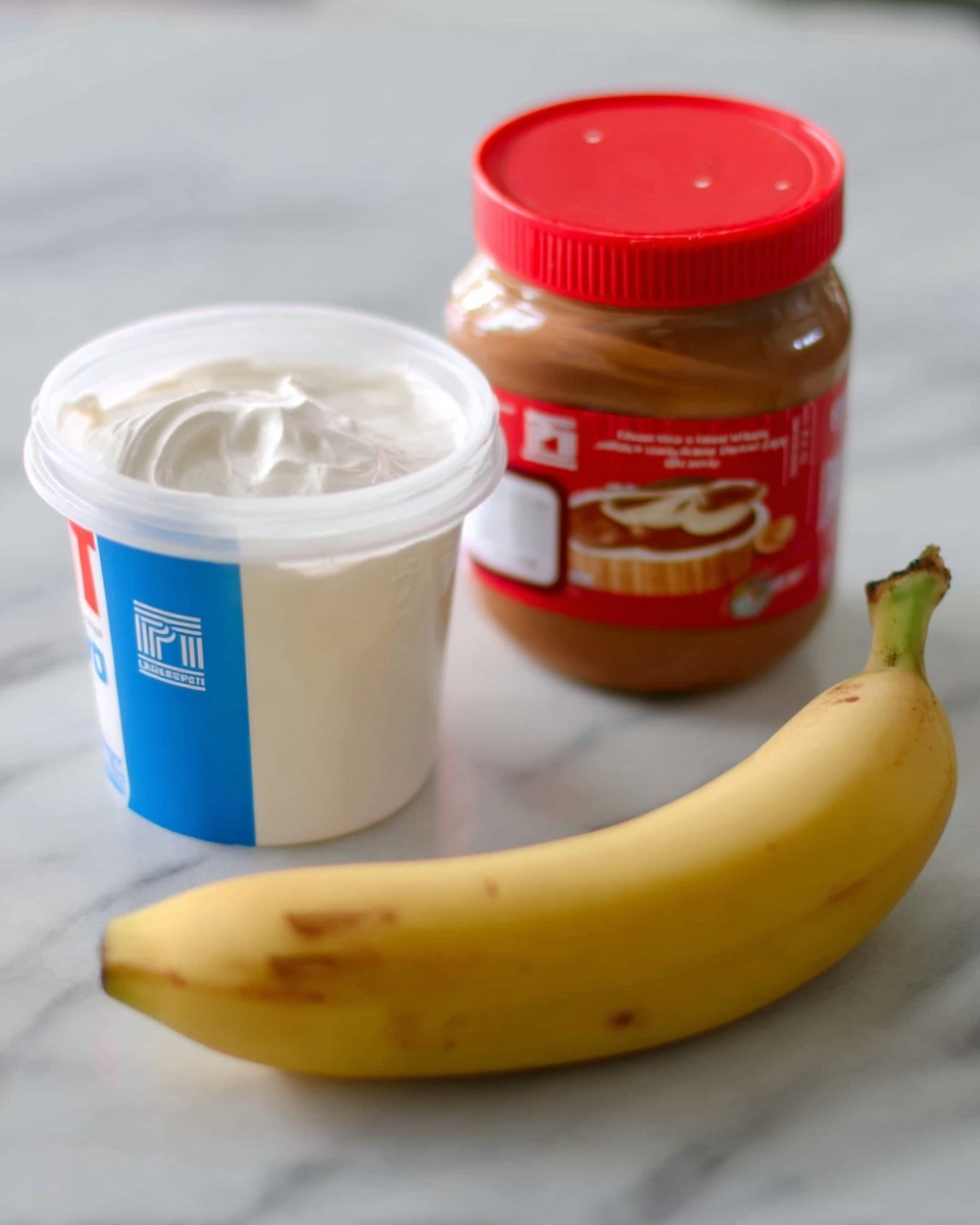 The image shows a white container of plain yogurt with a blue and red label on the left side, next to a jar of peanut butter with a red lid and a mostly red label on the right. In front of both containers, there is a whole ripe yellow banana lying horizontally on a white marbled surface. The yogurt container is open with yogurt visible inside. The photo taken with an iphone --ar 4:5 --v 7