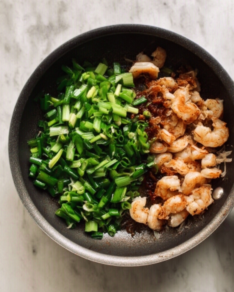 A top view of a cooking pan containing two main parts: on the right side, small pieces of cooked shrimp that are light pink with some browned edges, showing a slightly crispy texture; on the left side, fresh green chopped scallions with a crisp and vibrant look. The pan sits on a white marbled surface. Photo taken with an iphone --ar 4:5 --v 7