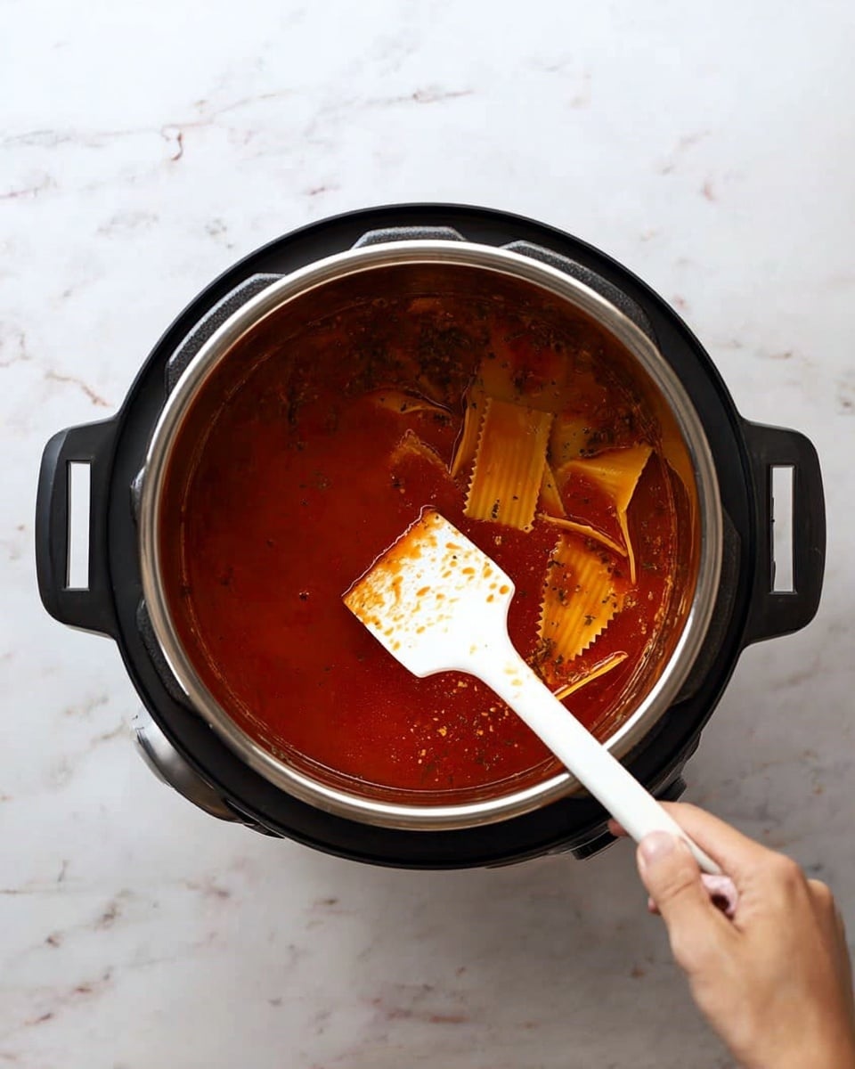 A black electric pot with a shiny inner silver pot filled with watery red sauce with visible herbs and orange wavy-edged pasta sheets floating on the surface. A woman's hand holds a white spatula with some sauce stains, stirring inside the pot. The pot sits on a white marbled surface. photo taken with an iphone --ar 4:5 --v 7