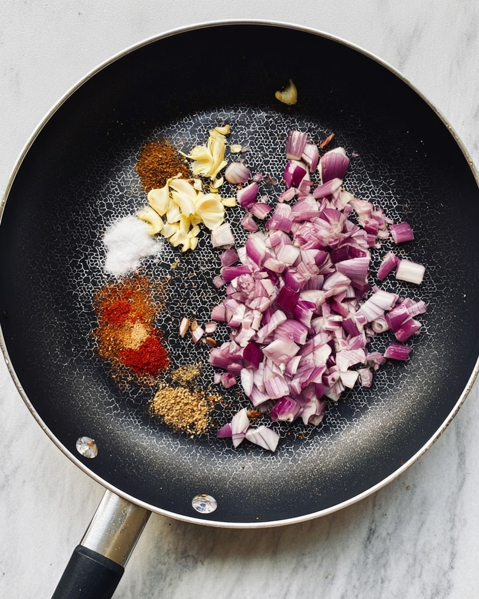 A black frying pan with a silver rim and black handle sits on a white marbled surface. Inside the pan, there are chopped red onions scattered mostly on one side, with small pieces of light yellow chopped garlic next to them. Several spices are laid out in small piles to the left of the onions and garlic, including white salt, red chili powder, light brown and darker brown powders. The pan has a honeycomb pattern at the center and the scene is lit with natural light. photo taken with an iphone --ar 4:5 --v 7