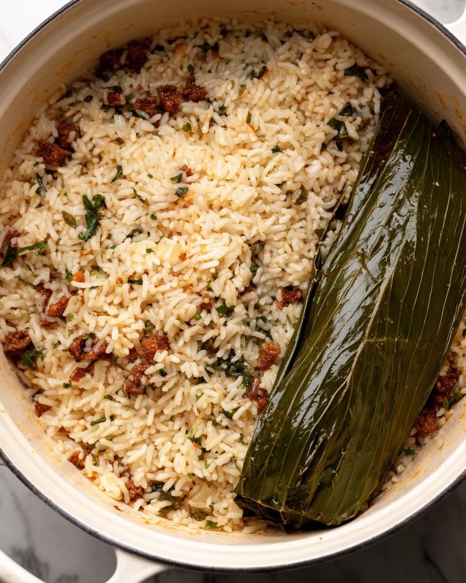 A close-up view of a white pot filled with cooked rice mixed with small pieces of browned meat and green herbs evenly spread throughout. One side of the pot shows a large dark green leaf, glossy with moisture, resting on top of the rice. The rice appears soft with a slightly oily texture, and the leaf adds a contrast with its smooth, shiny surface. The pot sits on a white marbled surface. photo taken with an iphone --ar 4:5 --v 7