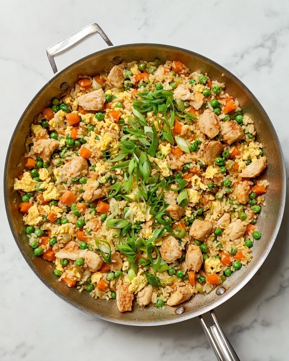 A skillet filled with cooked rice mixed with bright green peas and small orange carrot cubes, scattered with light yellow scrambled egg pieces and light brown chicken chunks. Thin slices of fresh green onions are spread on top, adding a fresh touch. The pan is silver with a metal handle and sits on a white marbled surface. The colors are warm and vibrant, showing a freshly cooked dish ready to serve photo taken with an iphone --ar 4:5 --v 7