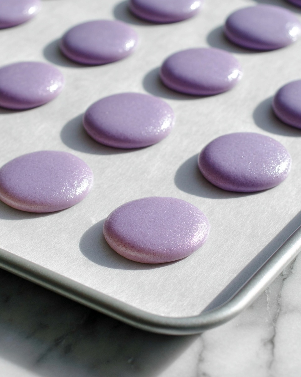 The image shows a baking tray with small, round, smooth, purple batter circles evenly spaced on white parchment paper. Each circle has a shiny, slightly thick texture and is about the same size, with a soft lavender color. The tray is placed on a white marbled surface that has subtle gray veins. The circles are rising a little, indicating they are ready to bake or set. The scene is well lit with natural light showing the glossy texture of the batter. photo taken with an iphone --ar 4:5 --v 7