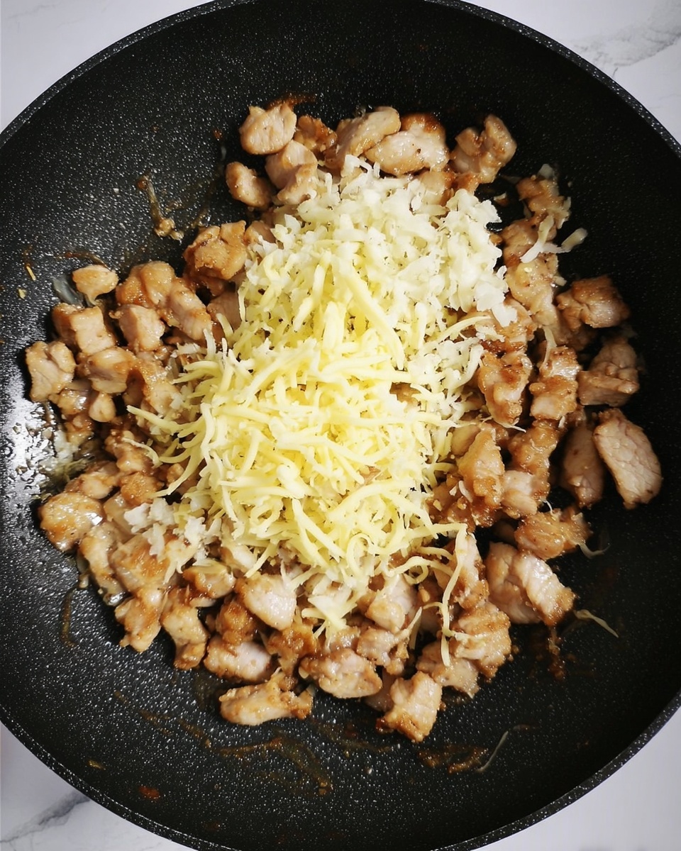 The image shows a black frying pan filled with small pieces of cooked pork that are light brown and slightly crispy. On top of the pork, there are two layers of finely chopped garlic in white and shredded cheese in pale yellow. The background surface is a white marbled texture. Photo taken with an iphone --ar 4:5 --v 7