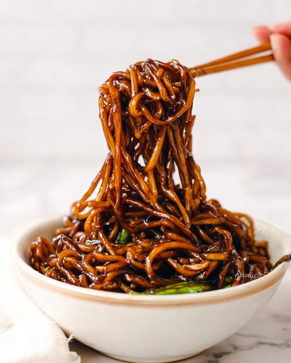 A close-up view of a white bowl filled with dark brown noodles covered in a thick glossy sauce, some green vegetable pieces mixed in. Thick noodles rise above the bowl, held by a pair of wooden chopsticks and a woman's hand reaching from the right, showing the noodles' smooth and shiny texture. The bowl sits on a white marbled surface, with a blurred white background. photo taken with an iphone --ar 4:5 --v 7