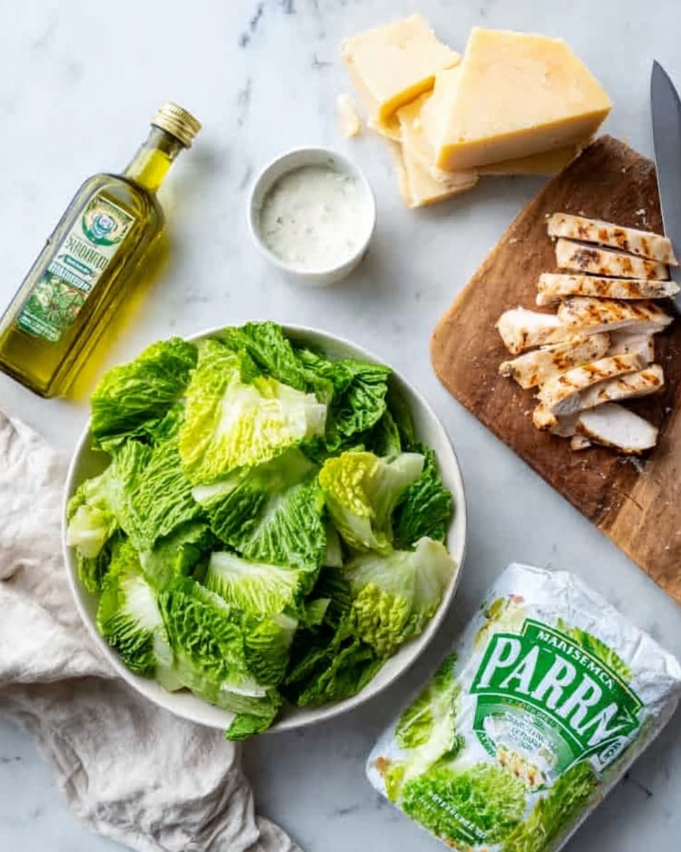 A white bowl filled with fresh green lettuce leaves that look crisp and slightly torn is placed on a white marble surface. Next to the bowl is a small white bowl with a white creamy dressing inside. There is a green and white package labeled