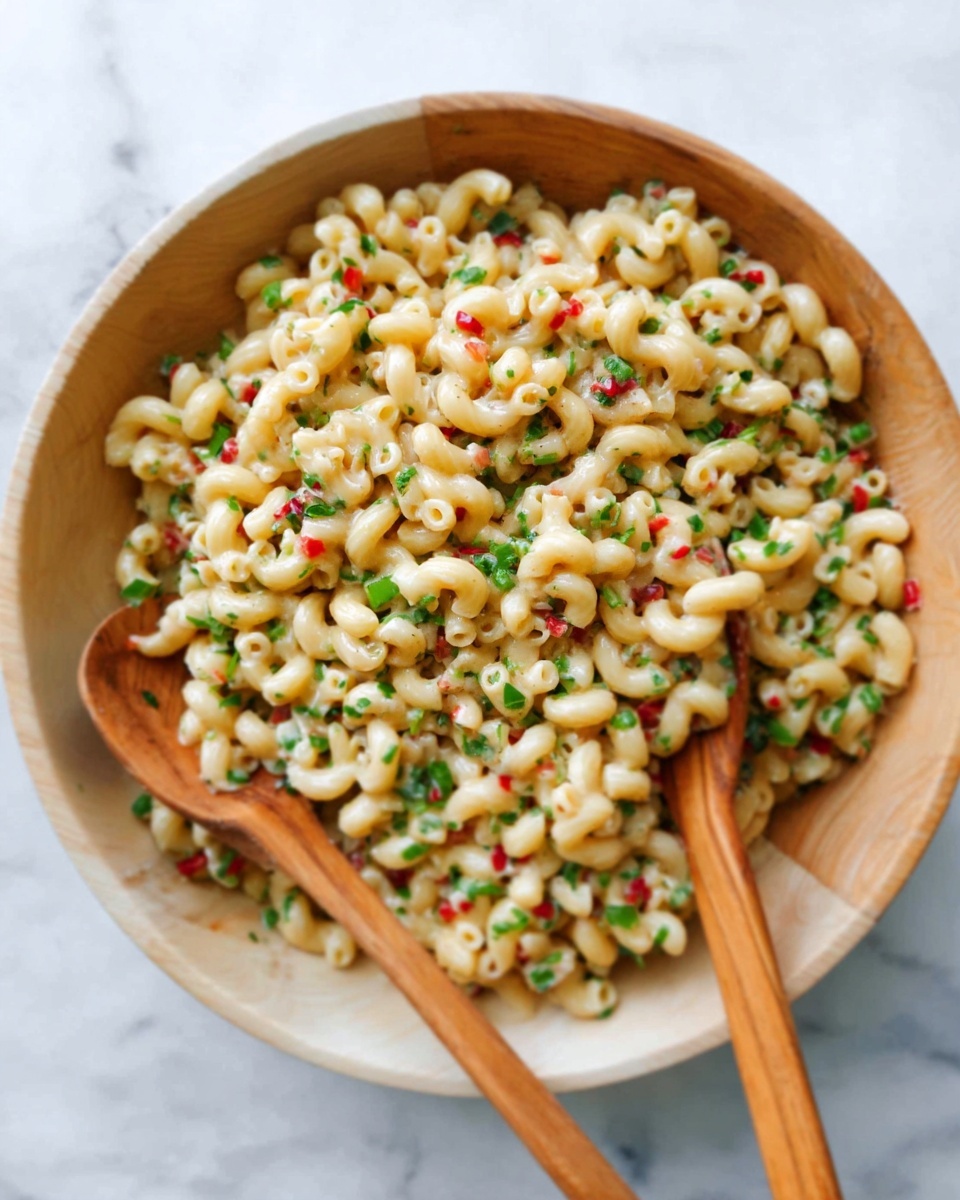 A white wooden bowl filled with cooked elbow macaroni pasta mixed with small pieces of green herbs and tiny red bits scattered evenly throughout. Two wooden spoons rest inside the bowl, one positioned on the left side and the other on the right, both partially buried in the pasta. The bowl sits on a white marbled surface. photo taken with an iphone --ar 4:5 --v 7