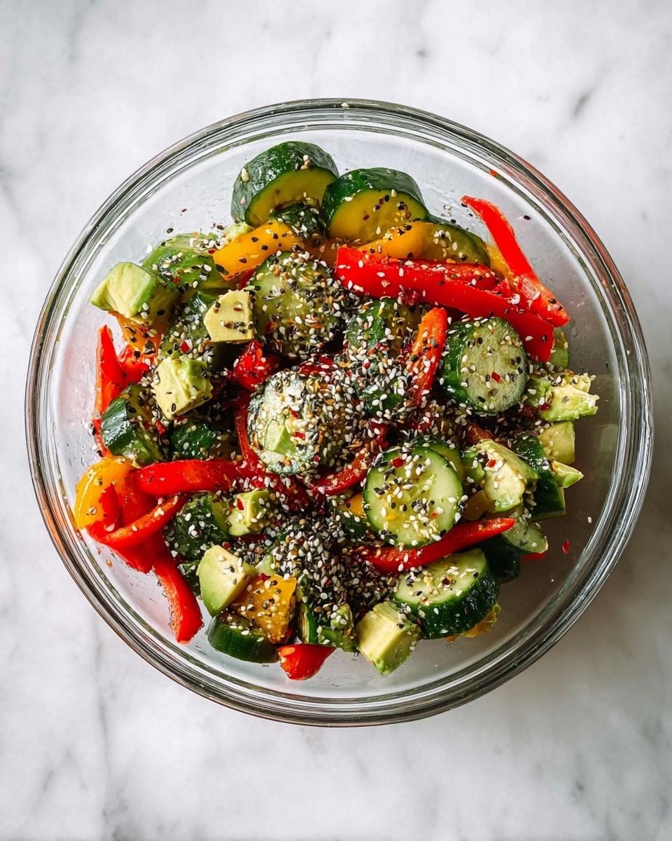 A clear glass bowl sits on a white marbled surface filled with a colorful salad. The toppings include thick, round slices of dark green cucumber with textured skin and soft interior, mixed with vibrant red and yellow pepper rings that add brightness and crunch. There are also small chunks of light green avocado tucked throughout the mix. The salad is sprinkled generously with a mix of white and black seeds, likely a seasoning blend, that adds texture and visual contrast over the fresh vegetables. photo taken with an iphone --ar 4:5 --v 7