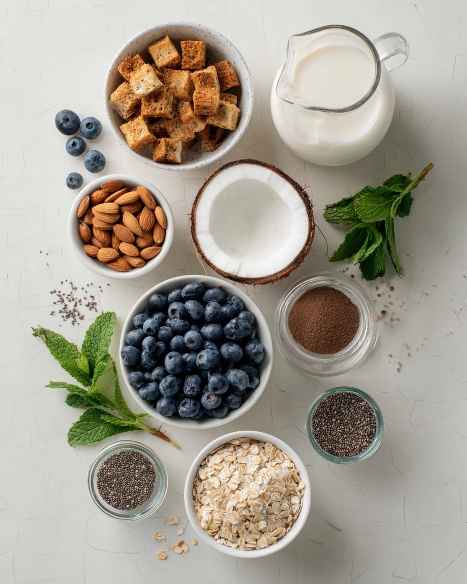 The image shows a white marbled surface with nine items arranged neatly: a white bowl filled with golden brown toasted bread cubes, a small white bowl with light brown almonds, a halved coconut with creamy white inside and brown shell, a bunch of fresh green mint leaves, a glass jug filled with fresh white milk, a white bowl filled with fresh blue blueberries, a white bowl containing fine white powder, a small glass jar with tiny black chia seeds, a white bowl of dark brown ground coffee, and finally a white bowl with light brown crumbled oats. A few blueberries and chia seeds are scattered on the surface around the bowls. photo taken with an iphone --ar 4:5 --v 7