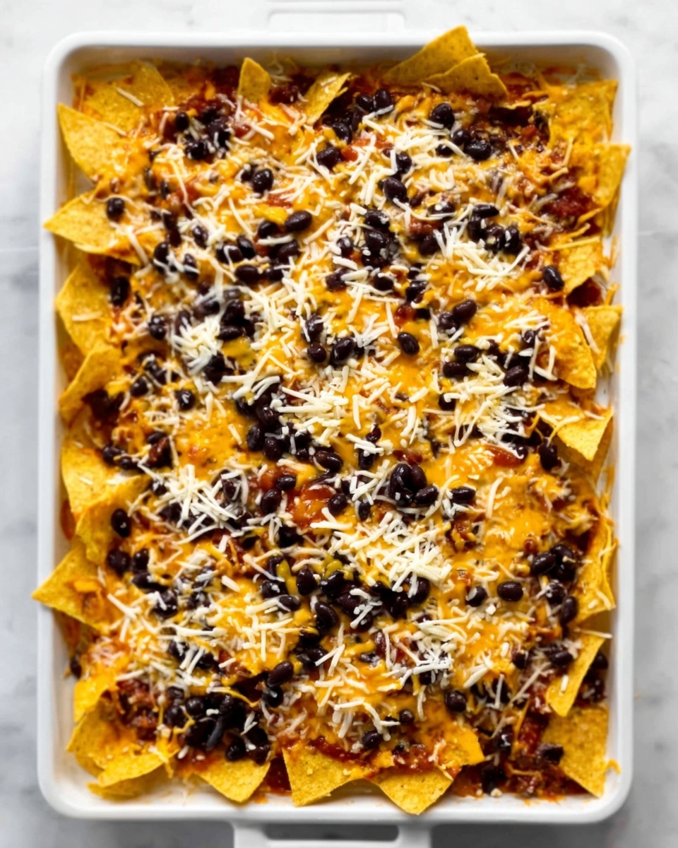 A white rectangular tray filled with a single even layer of triangular crisp yellow corn chips at the bottom. On top, a smooth orange melted cheese layer covers most chips. Scattered black beans form a separate uneven layer mainly on the upper right side. A thin layer of shredded white cheese spreads evenly across the entire dish as the last top layer. The tray is placed on a white marbled surface. Photo taken with an iphone --ar 4:5 --v 7