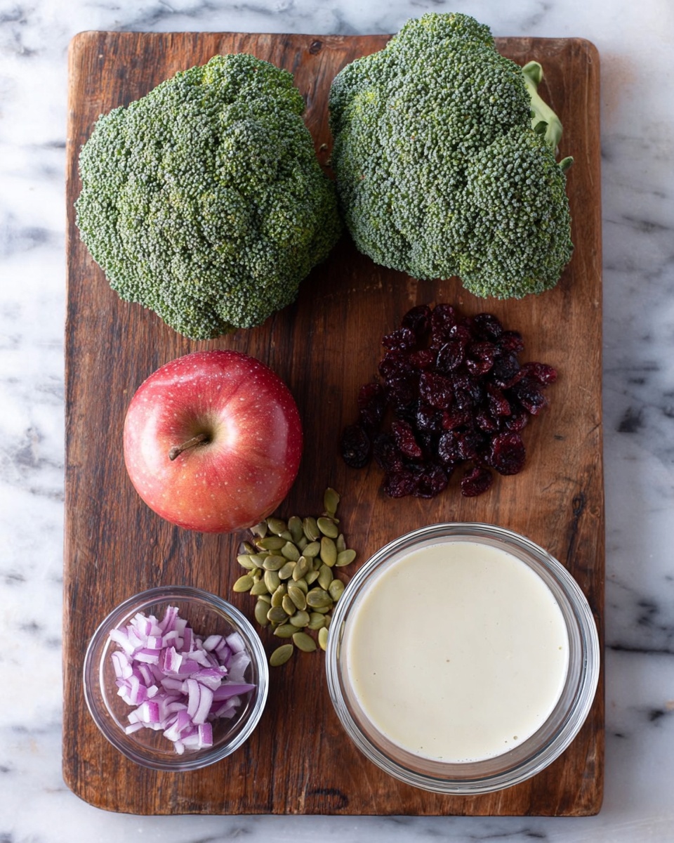 In the image, a dark wooden board rests on a white marbled surface. On the board, there are two fresh green broccoli heads placed side by side at the top. Below the broccoli, a round red apple sits on the left, and next to it on the right is a clear white bowl filled with a light cream sauce. At the bottom left of the board, a small clear bowl contains chopped purple onion pieces. To the right of the onion bowl, there is a small pile each of dark red dried cranberries and light green pumpkin seeds arranged neatly. The overall layout is clean and organized with natural colors. photo taken with an iphone --ar 4:5 --v 7