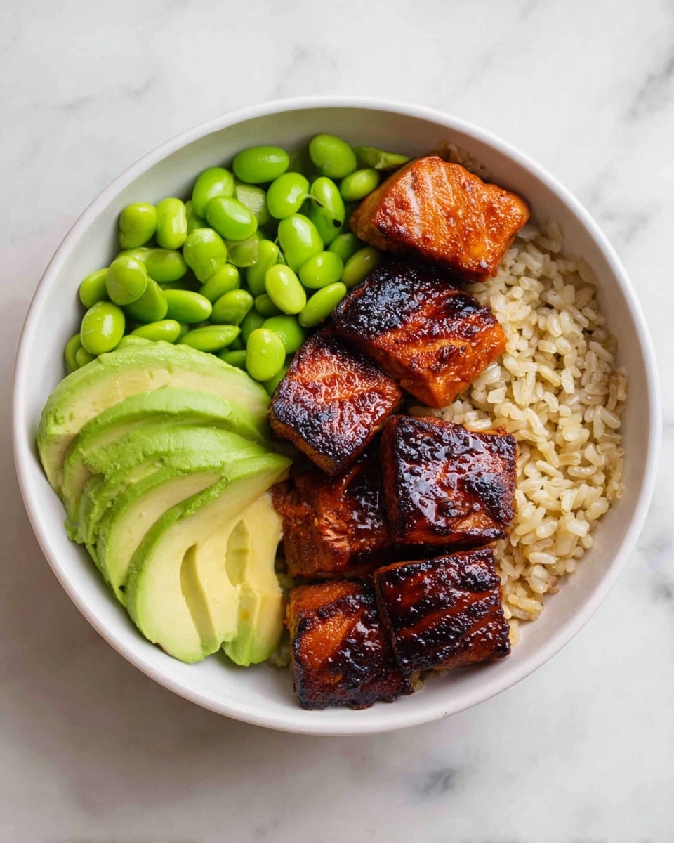 A white bowl filled with four main layers: at the bottom there is a layer of light brown rice with visible grains, on the right side there are six pieces of dark caramelized grilled salmon with a shiny texture, the top left side has a cluster of bright green, plump edamame beans, and the bottom left side shows three thick slices of pale green avocado arranged slightly overlapping. The bowl is placed on a white marbled surface. Photo taken with an iphone --ar 4:5 --v 7