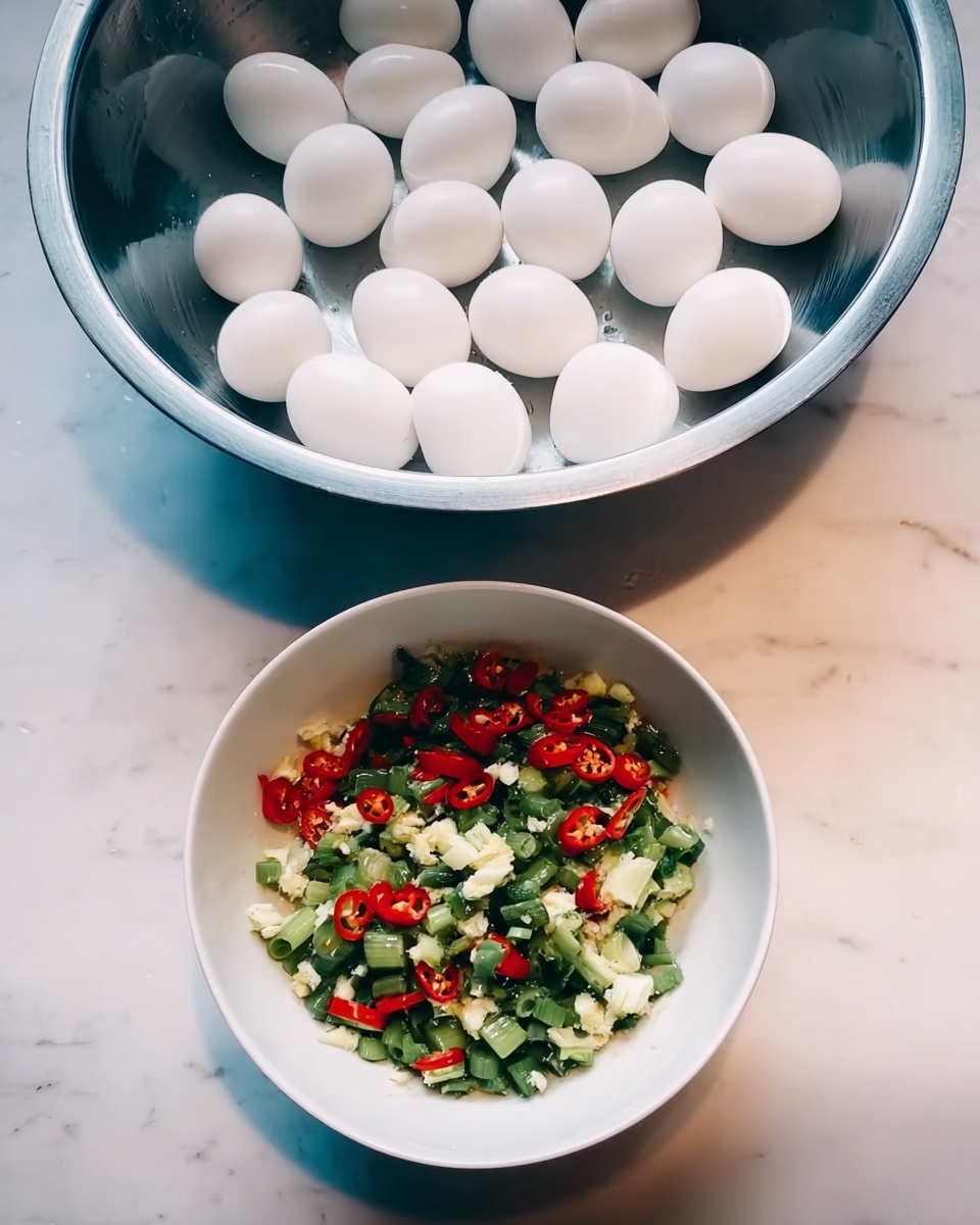The image shows two bowls on a white marbled surface. The top bowl is large and made of shiny metal, filled with many whole white eggs that have smooth shells and are closely packed. The bowl below is white and contains a colorful mix of chopped vegetables, featuring bright red chili slices, green spring onion pieces, and bits of white garlic, all combined evenly. The colors contrast nicely with the blueish tint inside the bowl. photo taken with an iphone --ar 4:5 --v 7
