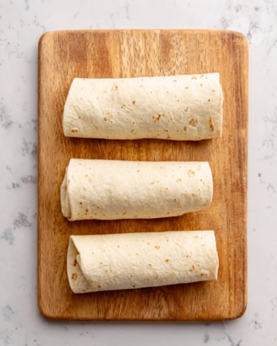 The image shows a wooden cutting board on a white marbled surface. On the cutting board, there are three rolled tortillas placed vertically in a row. Each tortilla is smooth and light beige with some small dark specks visible on the surface. The tortillas are evenly shaped, and the top one is slightly thinner compared to the other two. Photo taken with an iphone --ar 4:5 --v 7